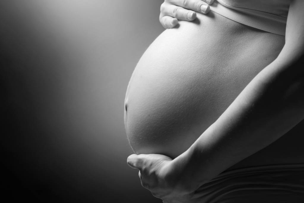 Close-up of a pregnant person’s belly with a hand resting above it