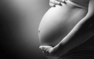 Close-up of a pregnant person’s belly with a hand resting above it